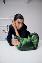 Person holding a green quilted handbag in a minimalistic setting