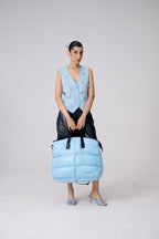 Woman holding a large blue puffer bag against a plain background