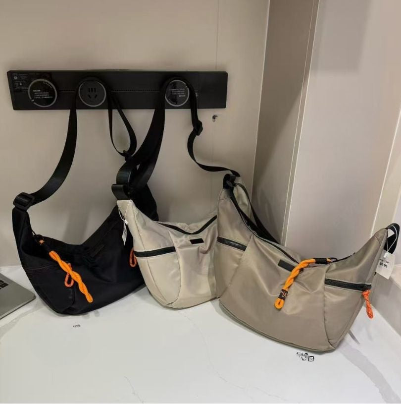 Three bags hanging on a wall hook against a white wall.Black bag with orange interior on a light gray background.Waterproof tote bag with a durable exterior and a bright orange interior. Features an adjustable strap and multiple pockets for organization. Ideal for travel, gym, or daily use in India.