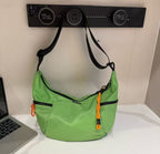 Green shoulder bag with black accents on a white surface next to a laptop.Waterproof tote bag with a durable exterior and a bright orange interior. Features an adjustable strap and multiple pockets for organization. Ideal for travel, gym, or daily use in India.