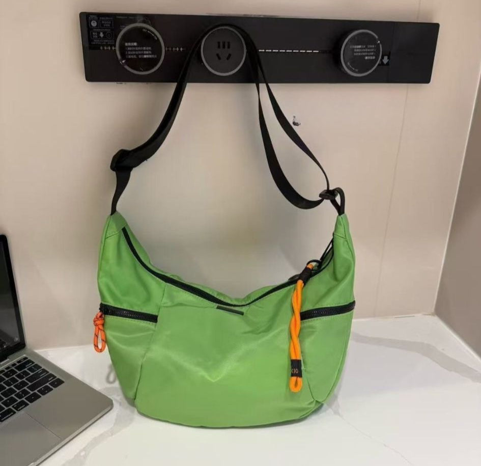 Green shoulder bag with black accents on a white surface next to a laptop.Waterproof tote bag with a durable exterior and a bright orange interior. Features an adjustable strap and multiple pockets for organization. Ideal for travel, gym, or daily use in India.