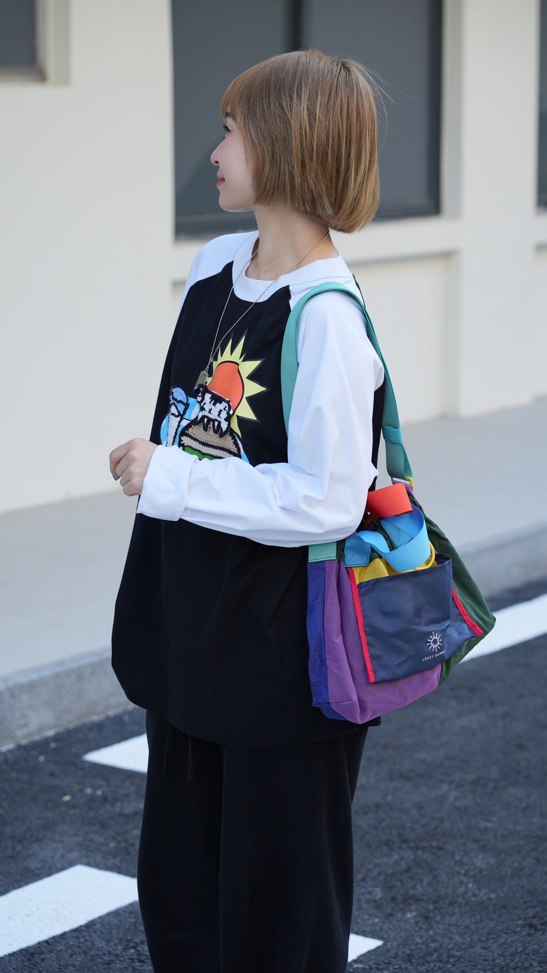 Person wearing a colorful bag with a multicolored design, standing on a street.