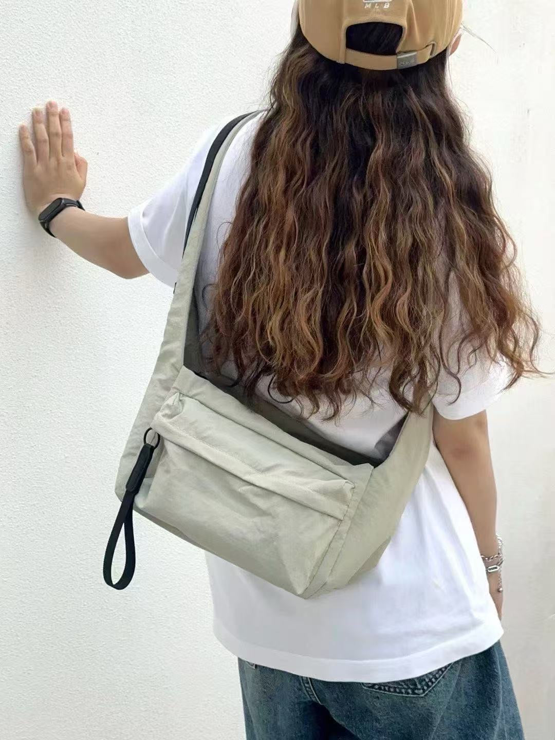 Person with long hair wearing a beige backpack against a white wall