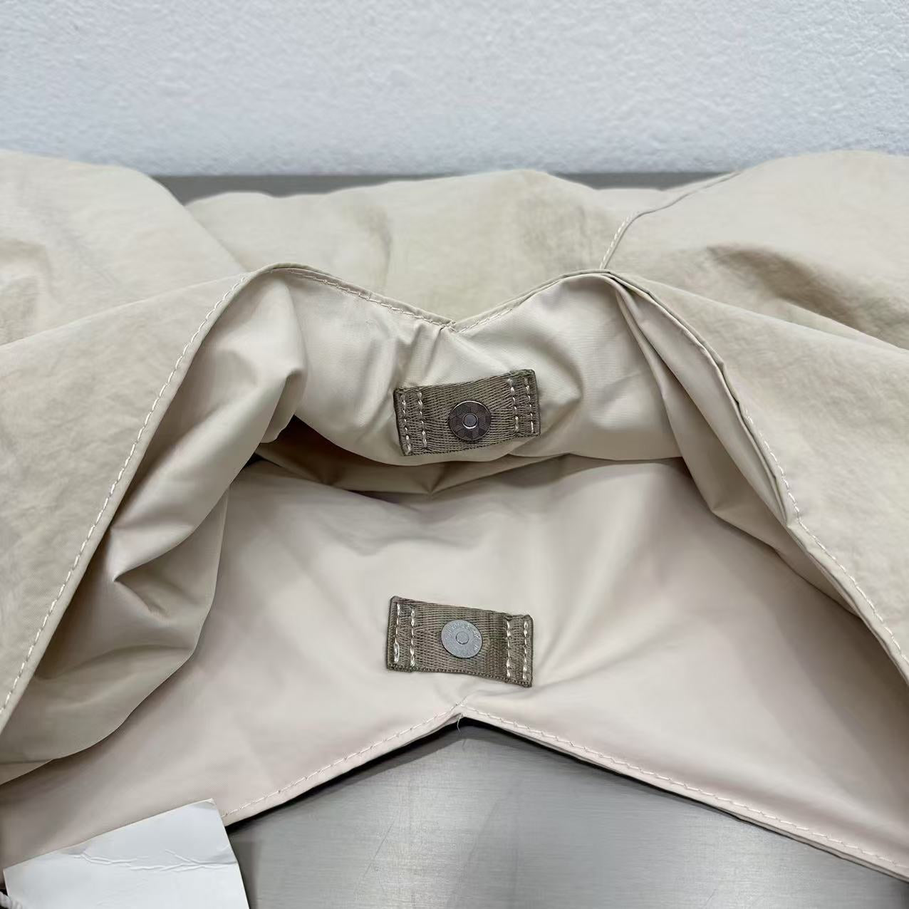 Close-up of a beige fabric with a button and label on a light gray background,Person holding a gray tote bag in an indoor setting,“Trendy tote bag for women in India with spacious design, inner pocket, and rope handle strap – perfect everyday alternative to Zara tote bags, H&M shopper bags, Mango handbags, Charles & Keith totes, Lifestyle handbags, Myntra handbags, and Fabindia casual totes.”