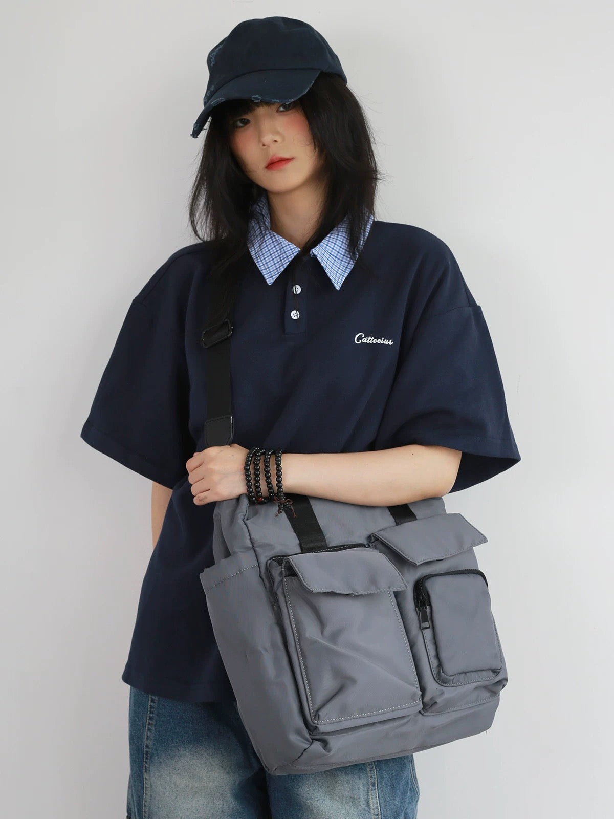 Person wearing a navy polo shirt and cap, holding a gray bag against a plain background