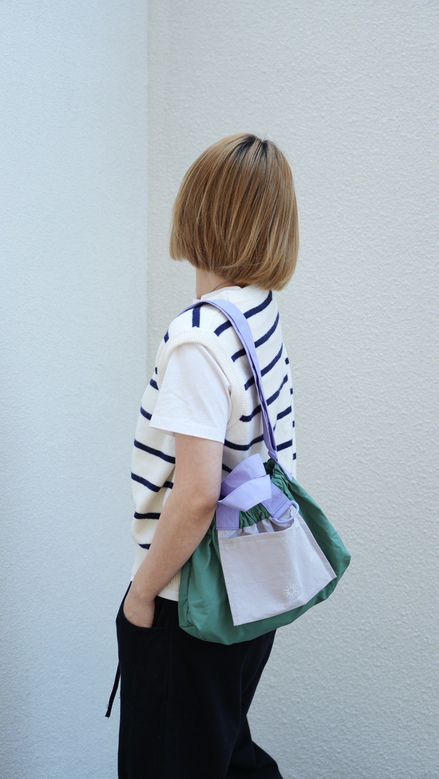 Person wearing a striped shirt and holding a green bag against a light background