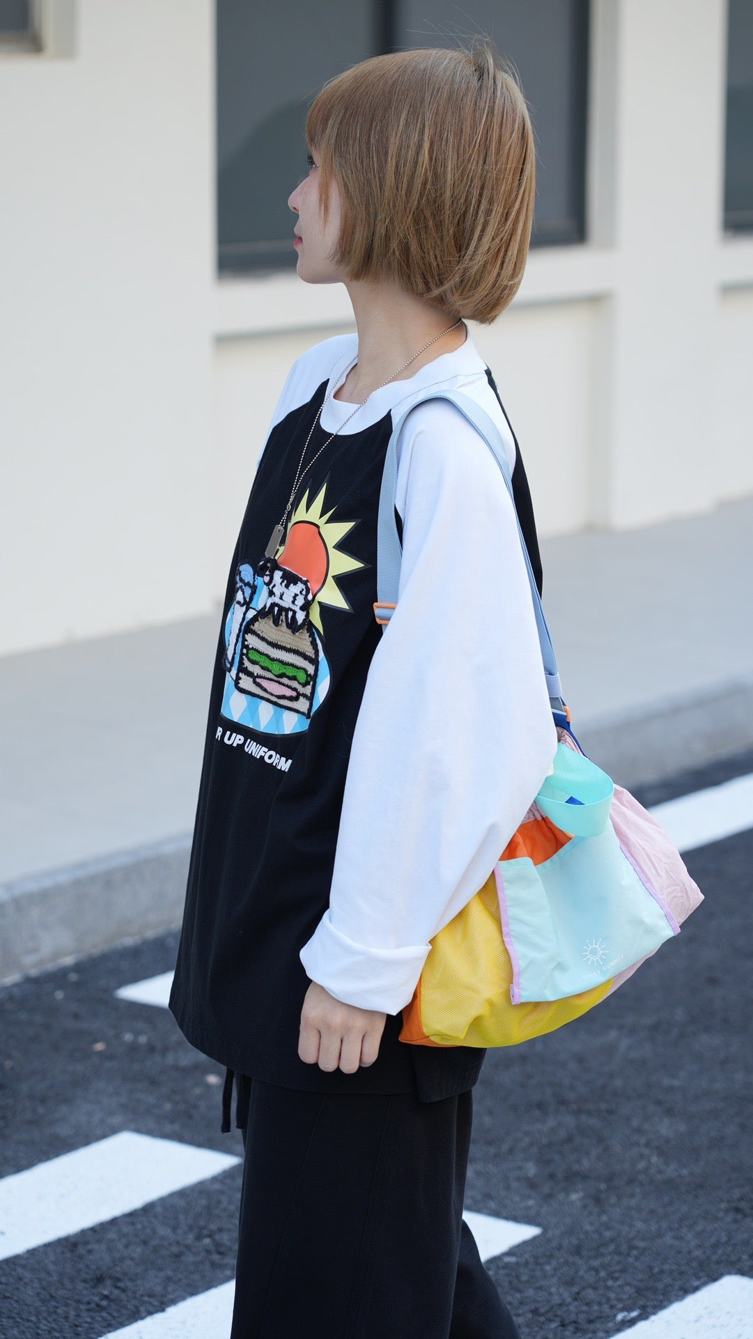 Person wearing a black hoodie with a colorful graphic design, holding a rainbow-colored bag.