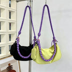 Two crescent-shaped shoulder bags hanging from a metal stand. One bag is black velvet with a purple braided strap, and the other is light yellow canvas with a matching purple braided strap.