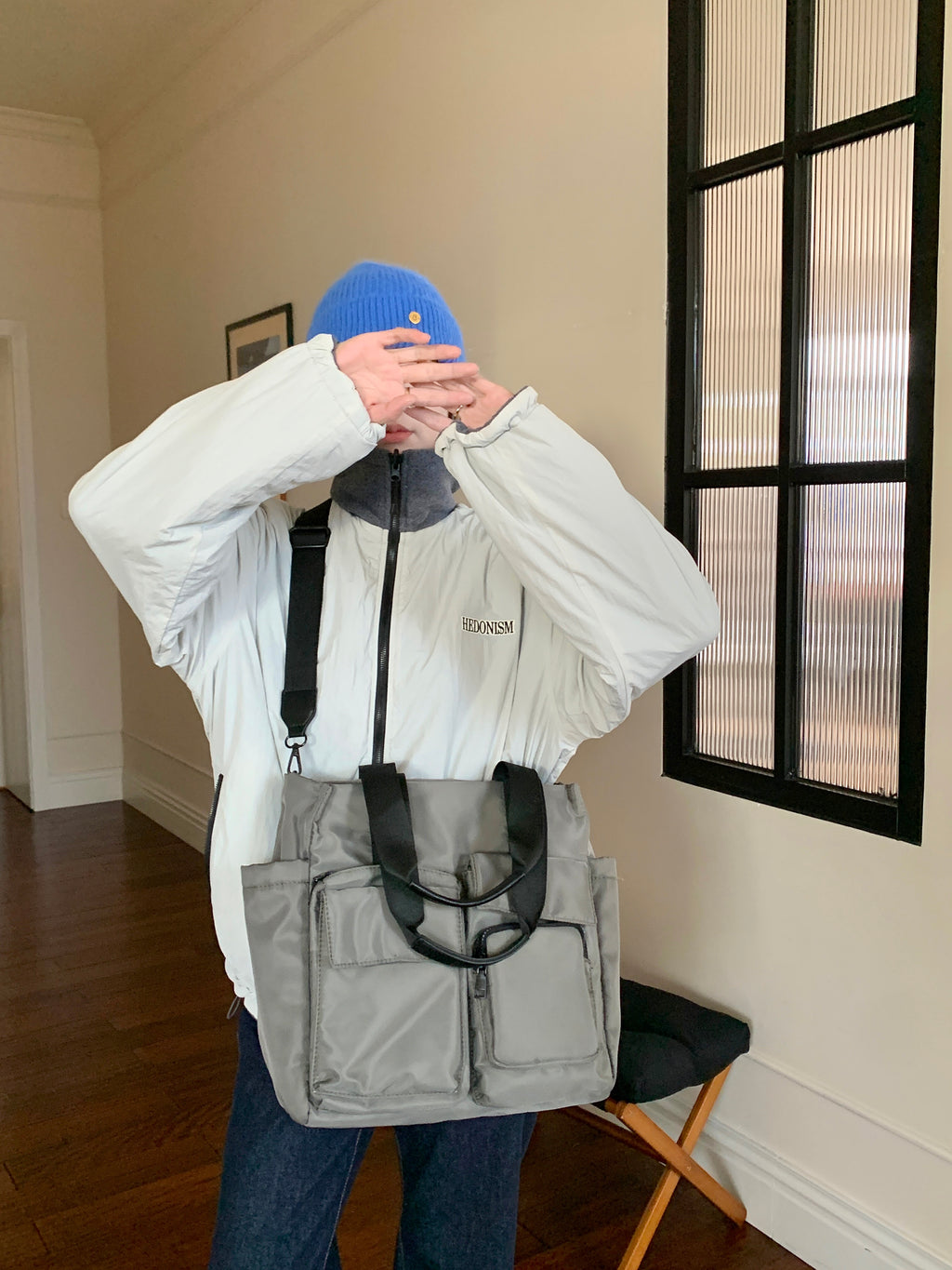 Person wearing a white jacket with a brand logo, gray backpack, and blue beanie indoors.