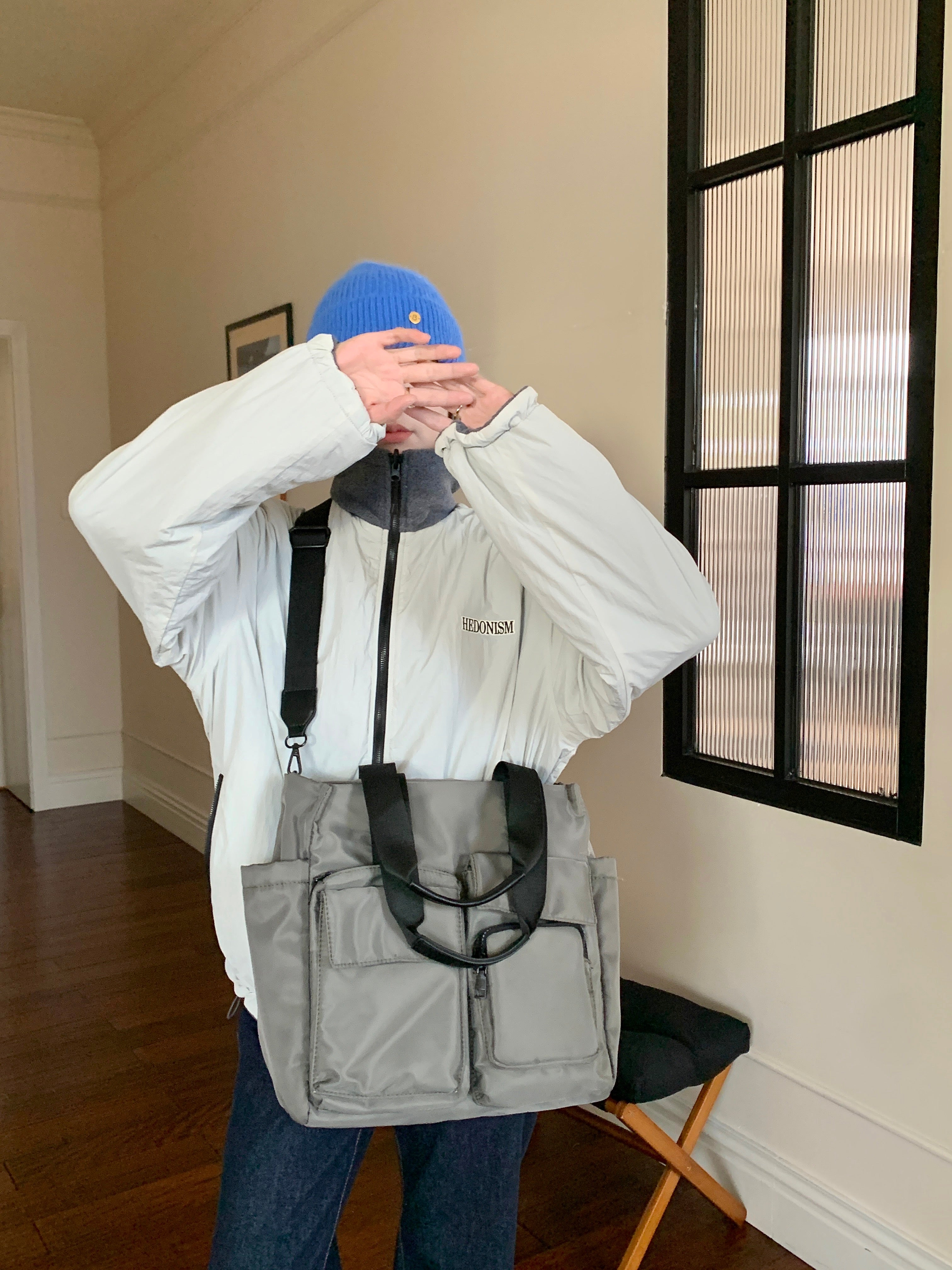 Person wearing a white jacket with a brand logo, gray backpack, and blue beanie indoors.