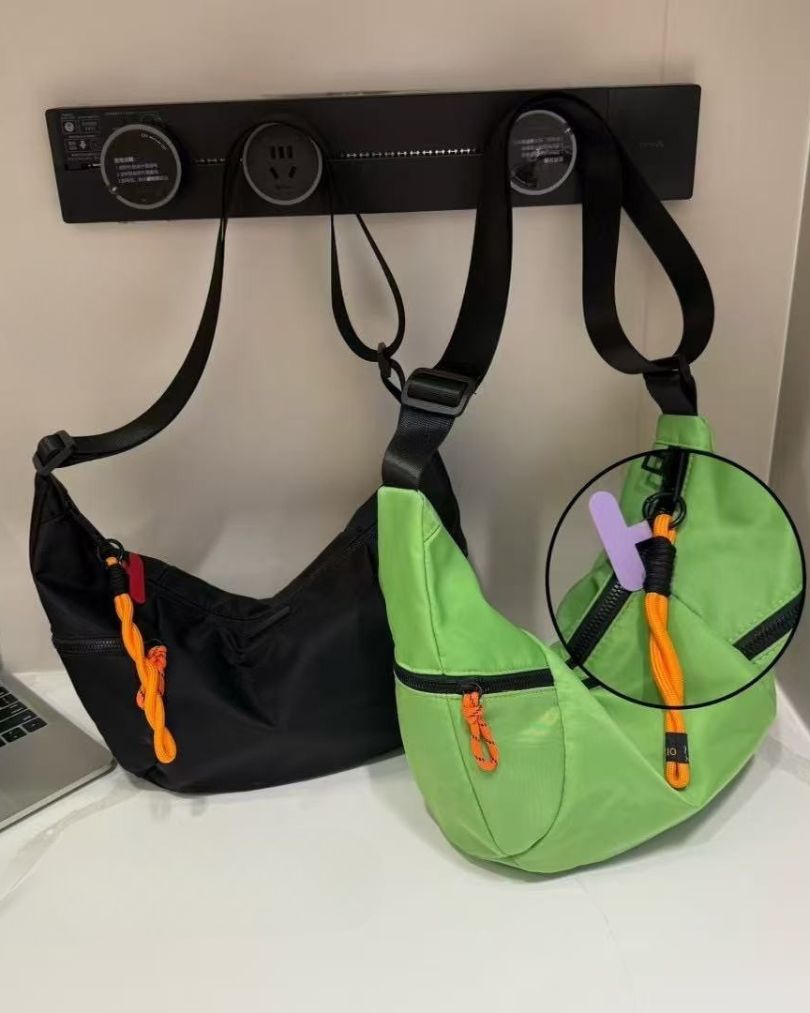 Black and green bags hanging on a wall-mounted hook with a laptop partially visible.Black bag with orange interior on a light gray background.Waterproof tote bag with a durable exterior and a bright orange interior. Features an adjustable strap and multiple pockets for organization. Ideal for travel, gym, or daily use in India.
