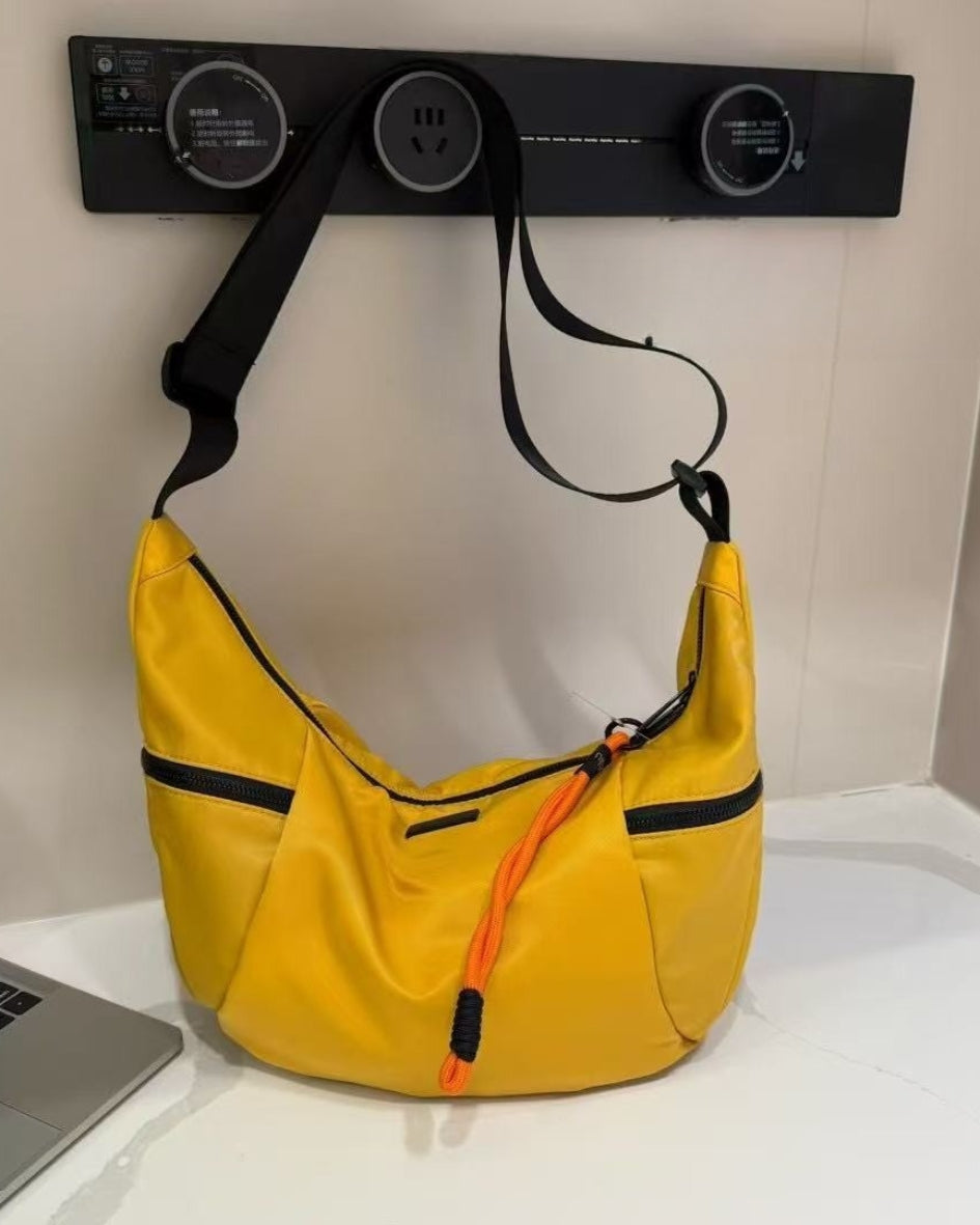 Yellow shoulder bag with black accents on a white surface next to a laptop. Waterproof tote bag with a durable exterior and a bright orange interior. Features an adjustable strap and multiple pockets for organization. Ideal for travel, gym, or daily use in India.