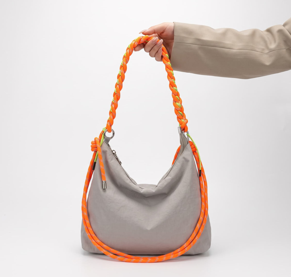 A light gray slouchy shoulder bag with thick braided orange straps, held by a person's hand against a clean white studio background.