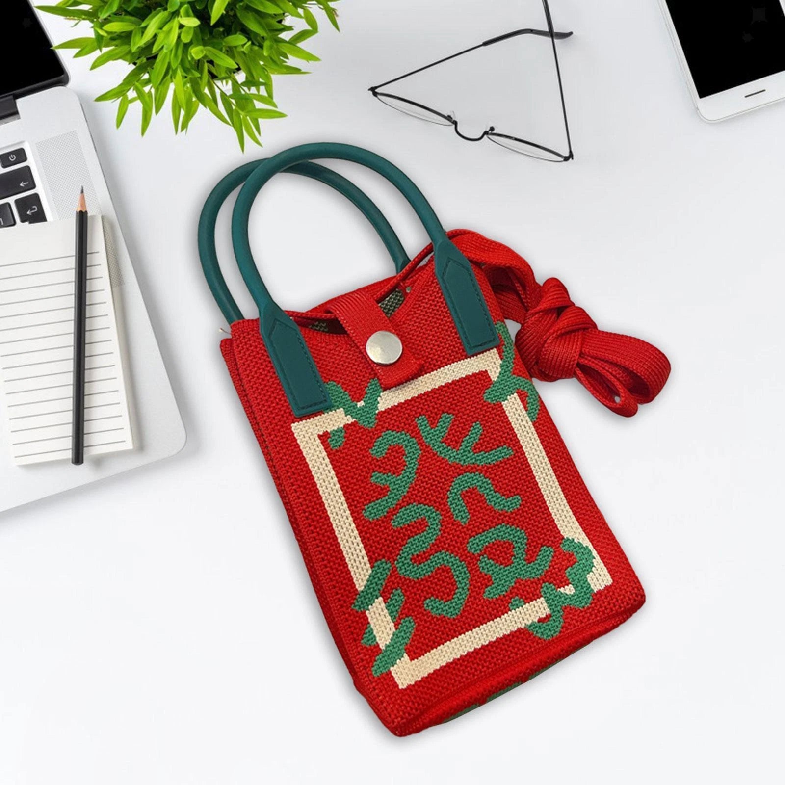 Red and green handbag on a white surface with office items in the background Handmade knitted sling bag with top handle and button closure, similar to products from Zouk, Chumbak, DailyObjects, The Souled Store, and India Circus, ideal for casual and everyday use.










